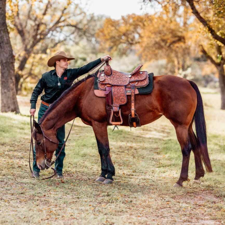 Molly's Custom Silver Cowboy handling the saddle of his horse in the forest